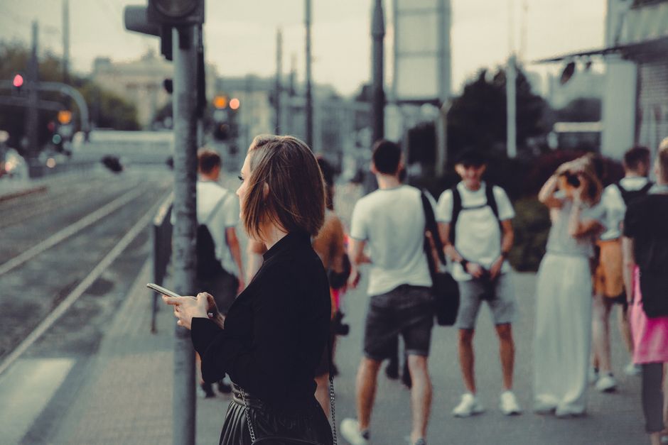 A stylish woman standing at a tram stop in Warsaw amidst busy city life.