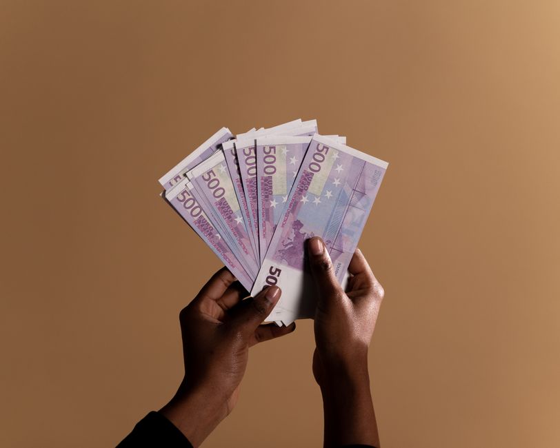 Close-up of hands holding several 500 euro banknotes against a neutral beige background, concept of wealth.