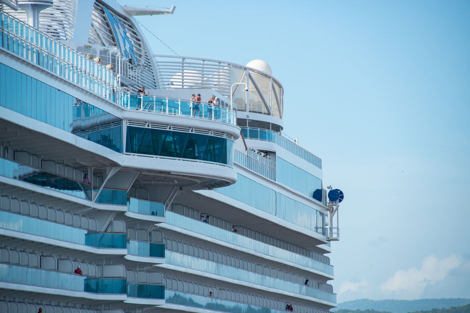 Close-up view of a modern cruise ship with people on deck, under a clear blue sky.