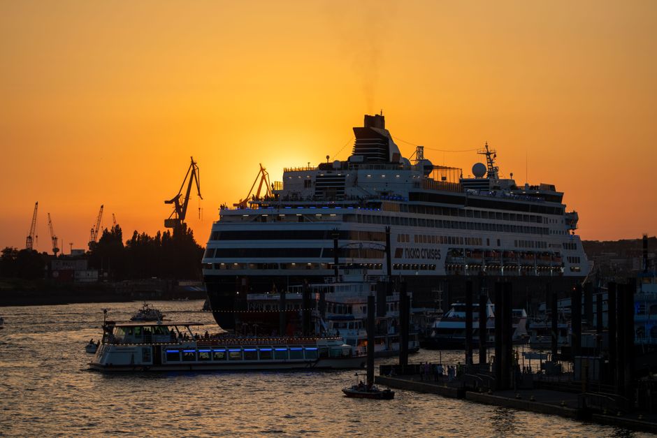 A majestic cruise ship docked at Hamburg harbor during a stunning sunset, with a golden sky.