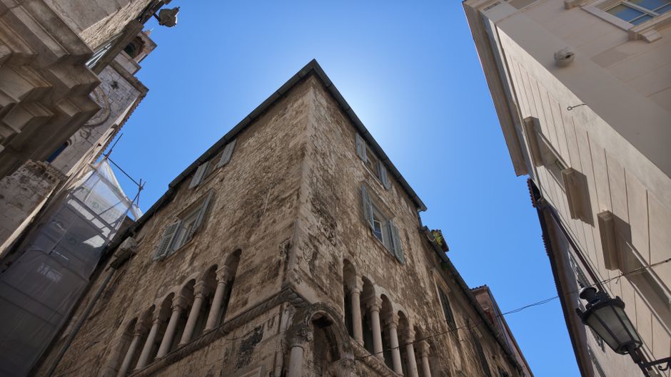 Historic stone building with ornate columns under a clear blue sky, showcasing medieval architecture.