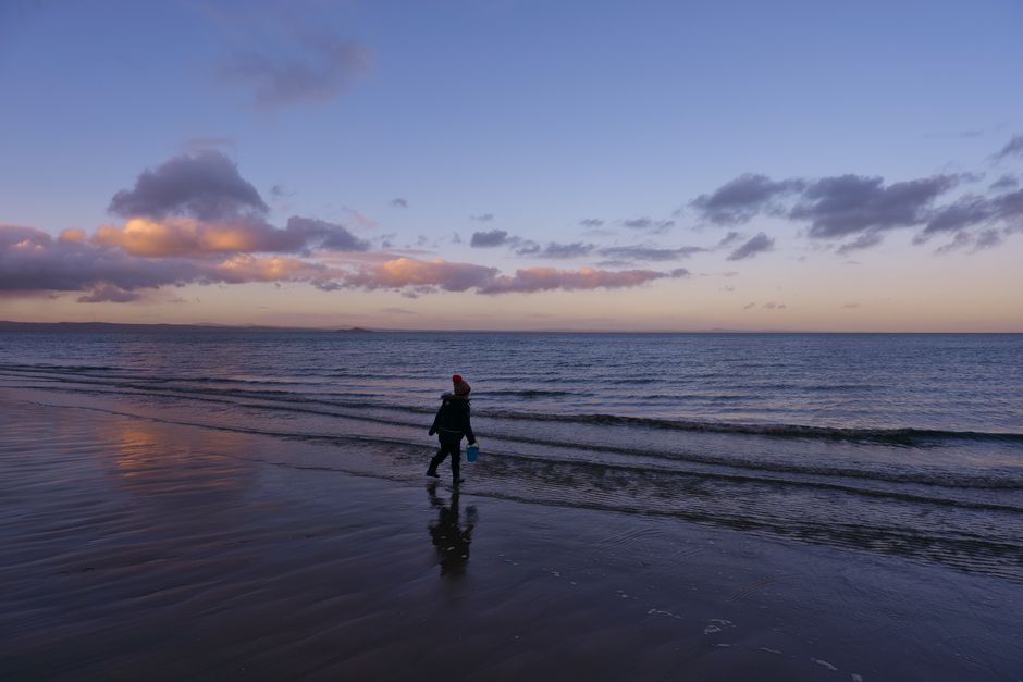 A child wearing a beanie walks along Portobello Beach, Edinburgh, during a beautiful sunset.
