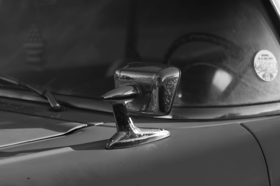 Close-up of a vintage car side mirror in black and white, evoking nostalgia.