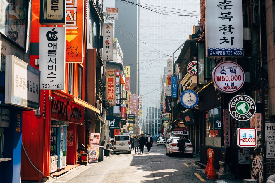 A bustling urban street in Seoul, filled with neon signs, shops, and pedestrians.