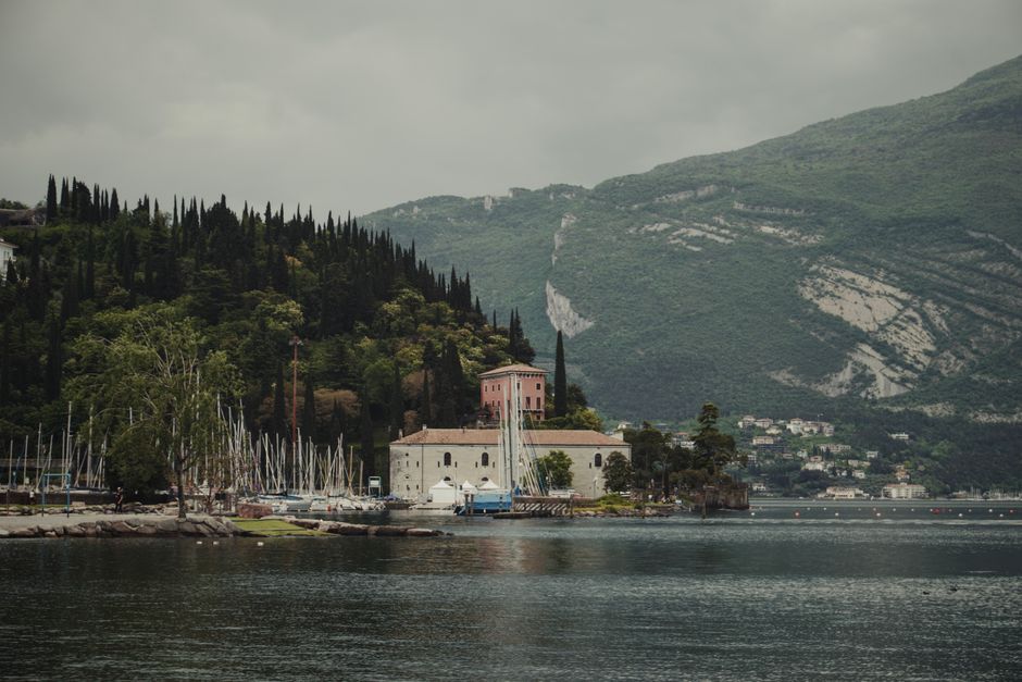 Picturesque view of a historic building by the water with lush greenery and sailboats.