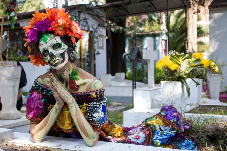 A vibrant Day of the Dead theme costume with skeletal face paint in a cemetery setting.