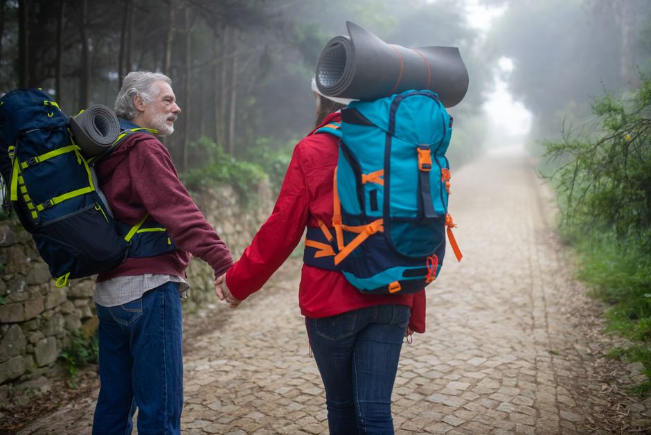 An elderly couple hiking hand in hand through a foggy path surrounded by nature in Portugal.