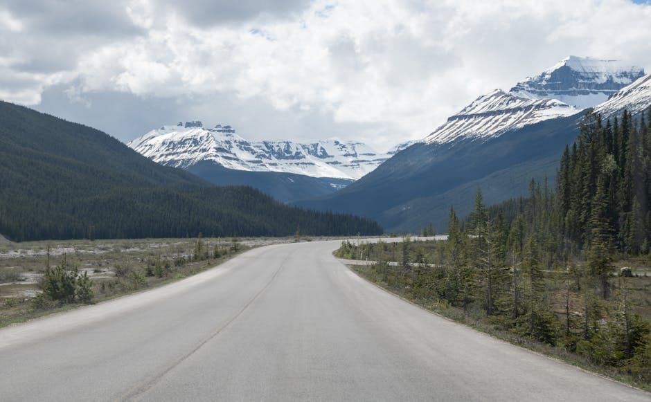 A picturesque road leading towards stunning snowcapped mountains under a cloudy sky.