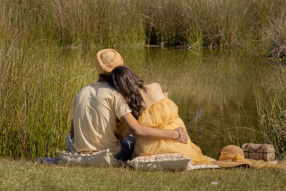 A couple enjoying a peaceful moment together by a serene pond, surrounded by tall grass.