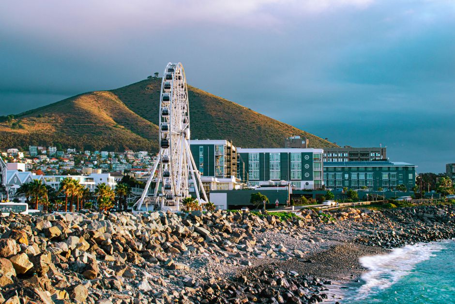 A picturesque view of Cape Town's coastline featuring the Cape Wheel, mountains, and cloudy skies.