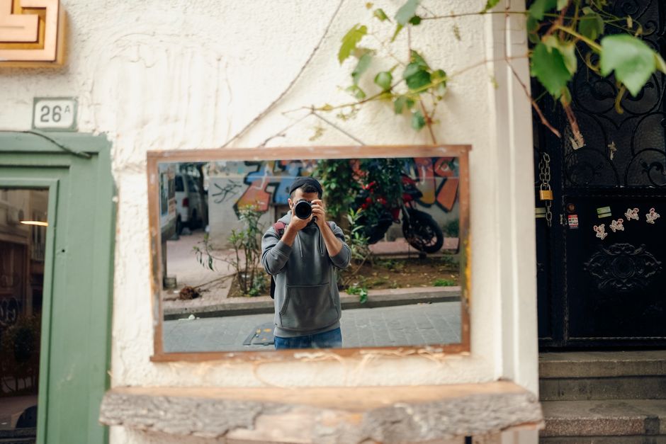 A photographer captures his reflection in a street mirror surrounded by urban graffiti.