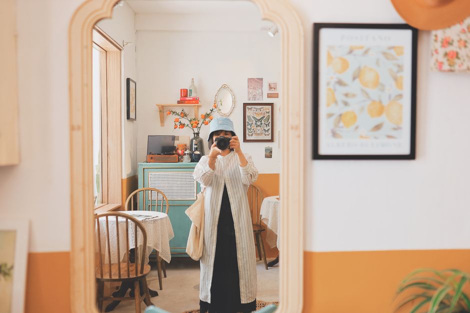 A woman takes a photo of her reflection in a chic, cozy café mirror setting.