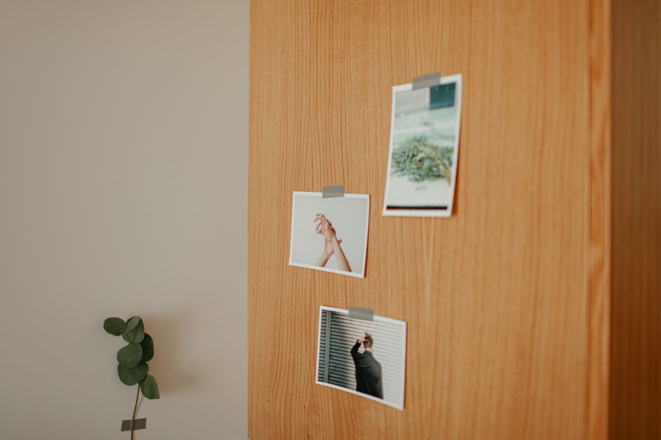 A minimalist wooden wall featuring taped photographs and a small plant, creating a cozy decor.