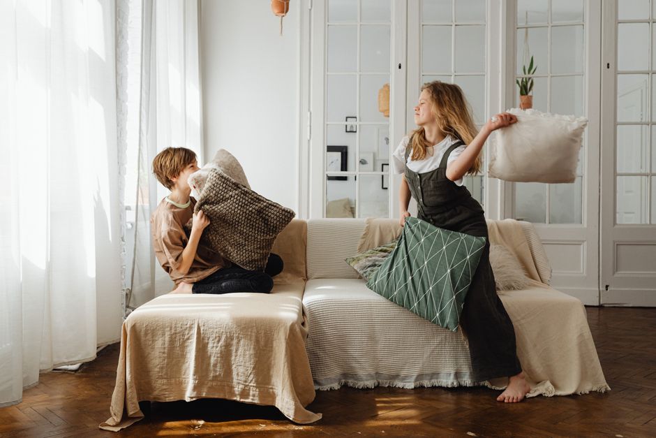 Two teenagers joyfully engaged in a playful pillow fight at home, enhancing bonds and fun.