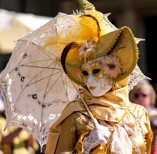 Intricate yellow masquerade costume and mask with parasol at carnival