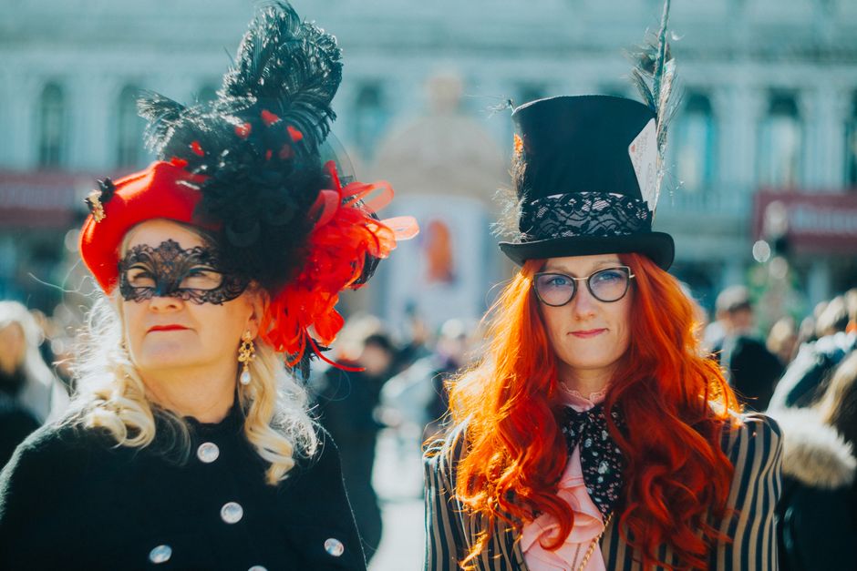 Women in vibrant carnival costumes and ornate hats at a Venetian festival, showcasing unique style and tradition.